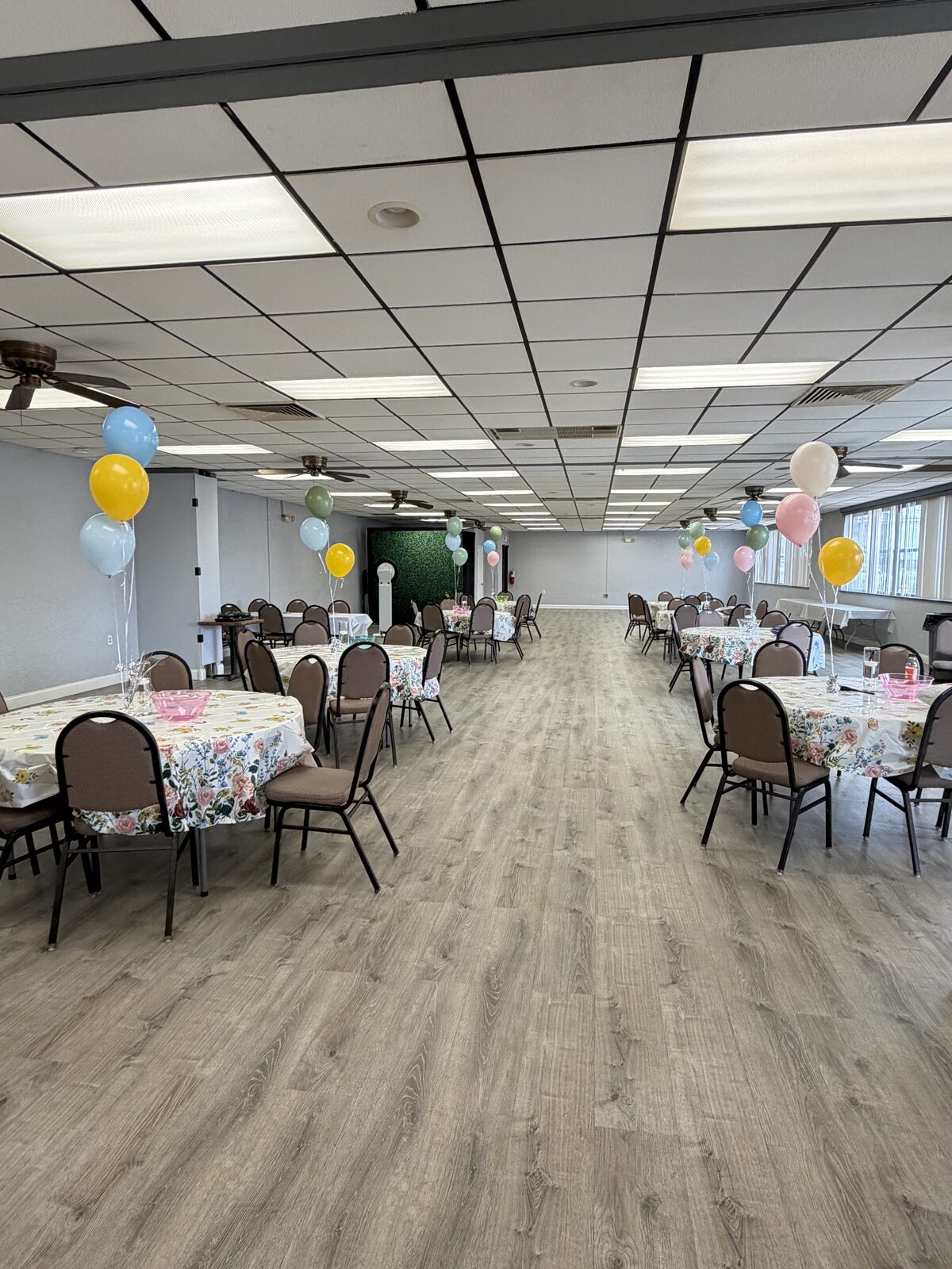 Wide view of the hall with floral tablecloths and pastel balloon bundles